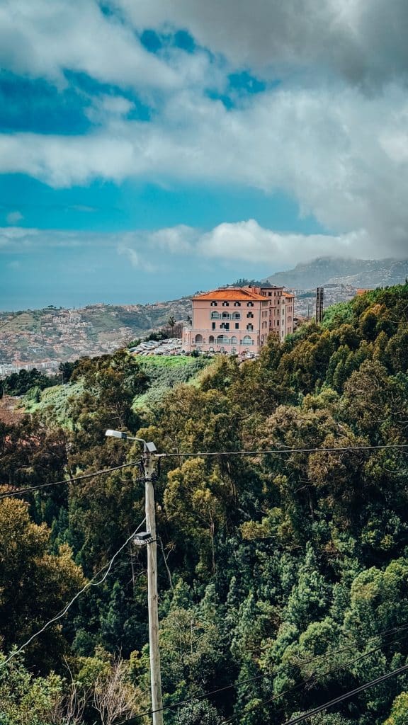 Das ehemalige Hotelgebäude des Monte Palace (innen nicht zu besichtigen) vom Garten aus, dahinter die Hügel von Funchal. Foto: Ewelina Podrez-Siama 2025