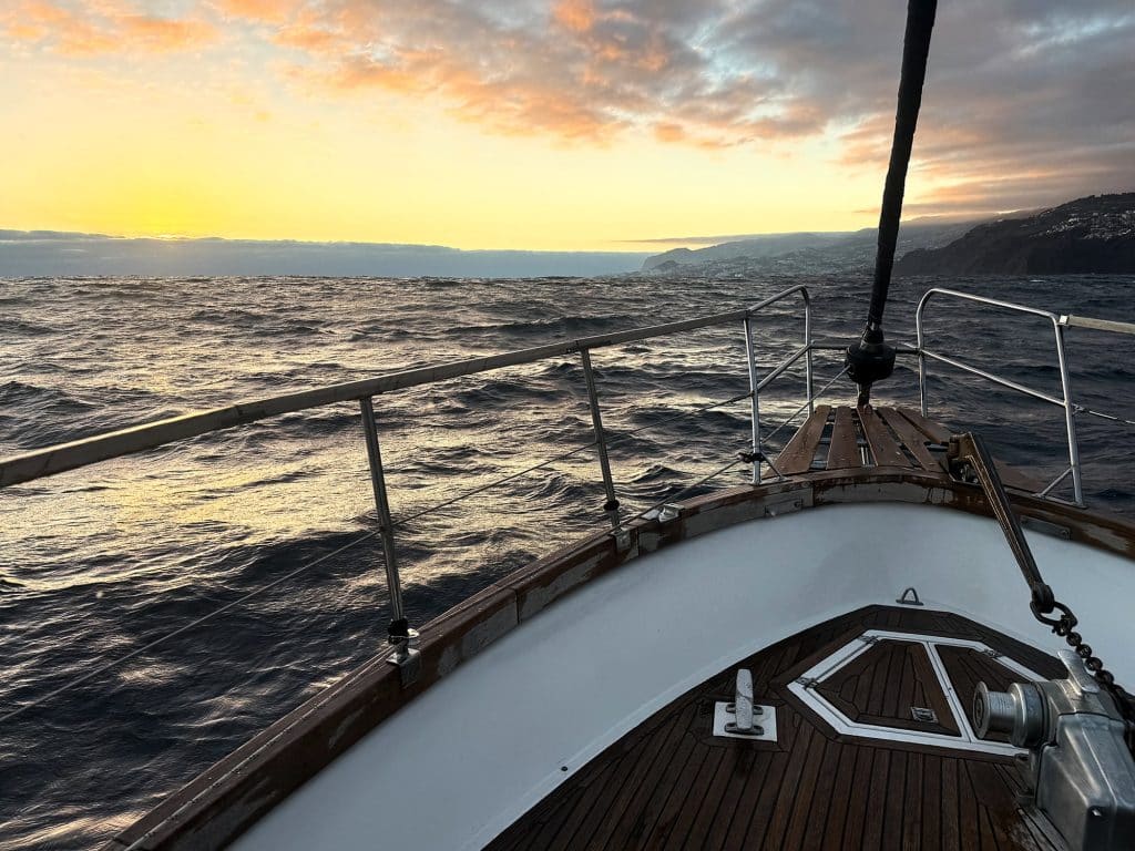 Holzdeck und Bug einer Jacht auf bewegtem Meer bei Sonnenuntergang