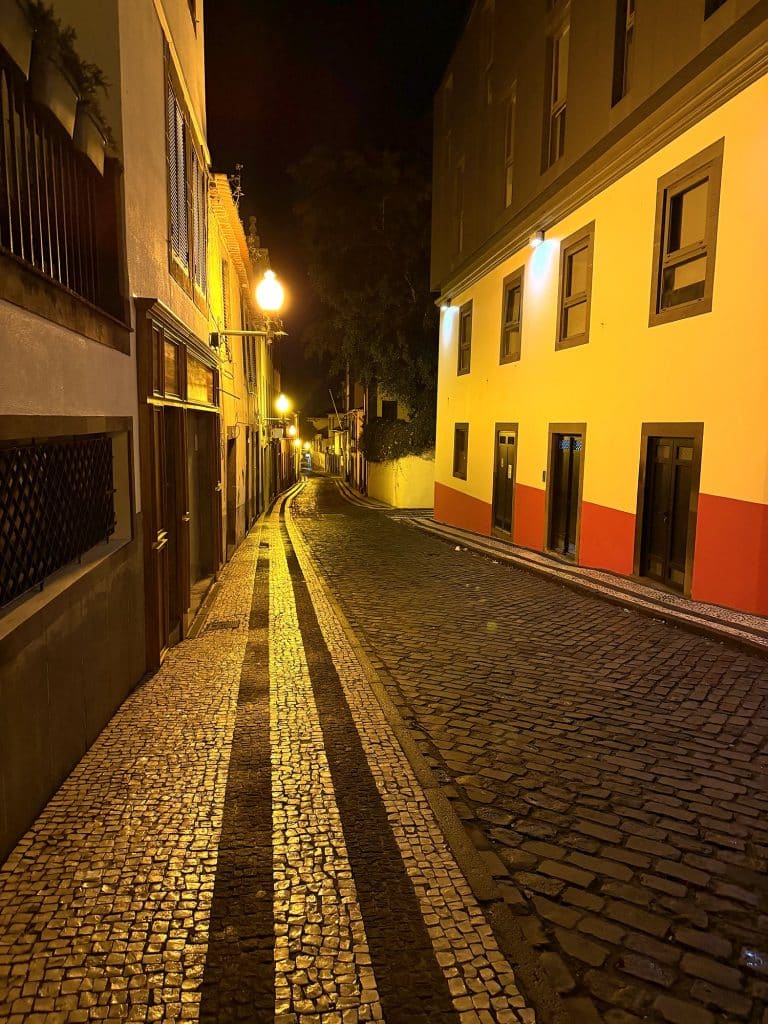 Eine leere gepflasterte Gasse in Funchal nachts im Laternenlicht