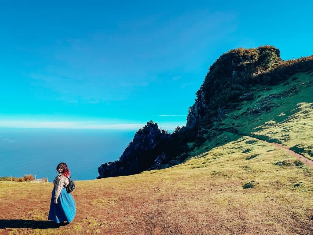 Frau auf einem Pfad über die Hochebene, im Hintergrund das Meer und hohe Felsen