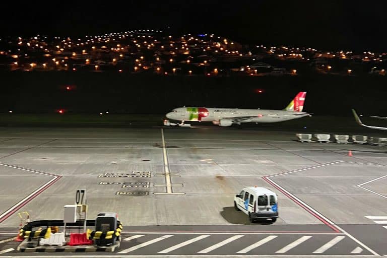 Ein TAP-Flugzeug nachts auf dem Vorfeld des Flughafens Madeira, dahinter die Lichter der Häuser am Hang