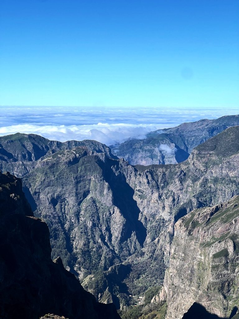 Steile, zerklüftete Täler und Kämme im Zentrum Madeiras, darüber ein Wolkenmeer und blauer Himmel