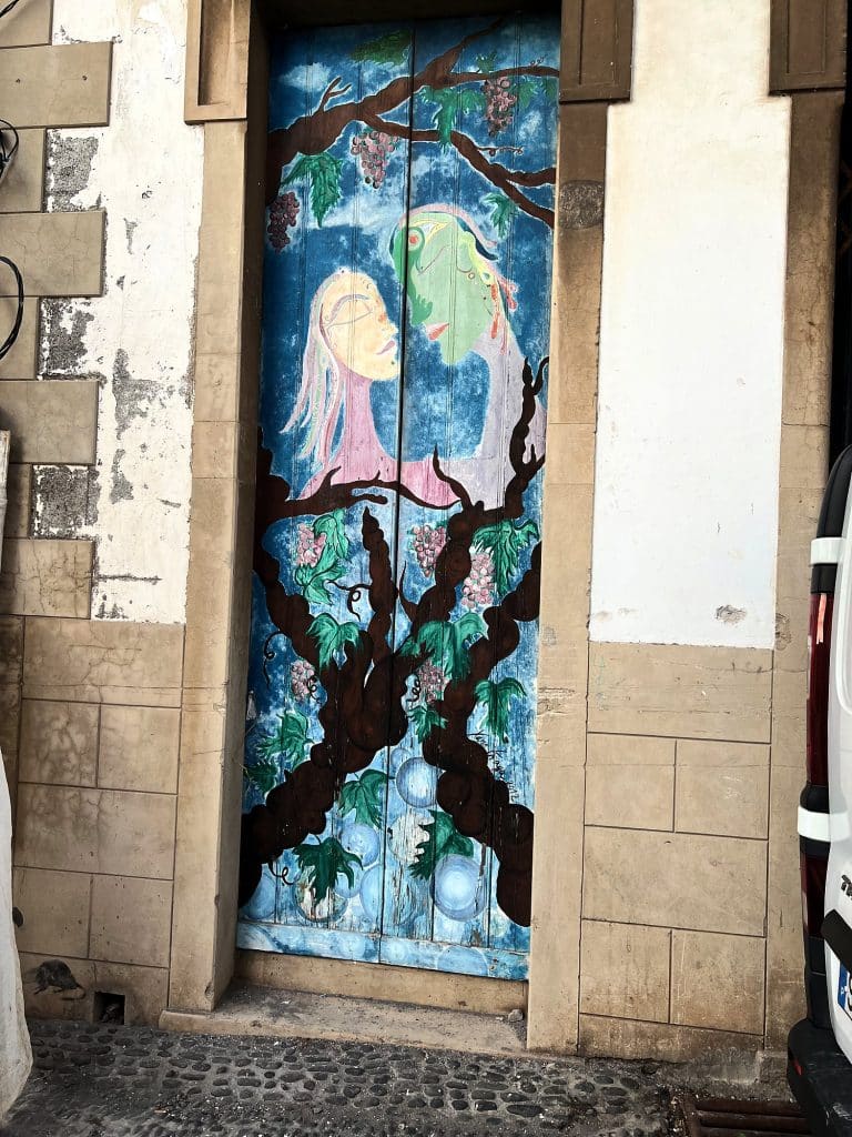 Eine Tür, bemalt mit einem Baum und zwei Figuren auf blauem Grund, im Steinrahmen eines alten Stadthauses