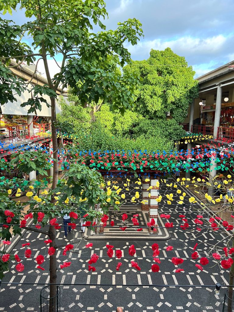 Der Innenhof der Markthalle Mercado dos Lavradores mit Mosaikboden, darüber Reihen bunter Deko in Blumenform, ringsum Galerien mit Ständen