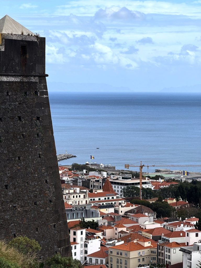 Der dunkle Steinturm der Fortaleza do Pico über den Dächern des Zentrums von Funchal und dem Ozean