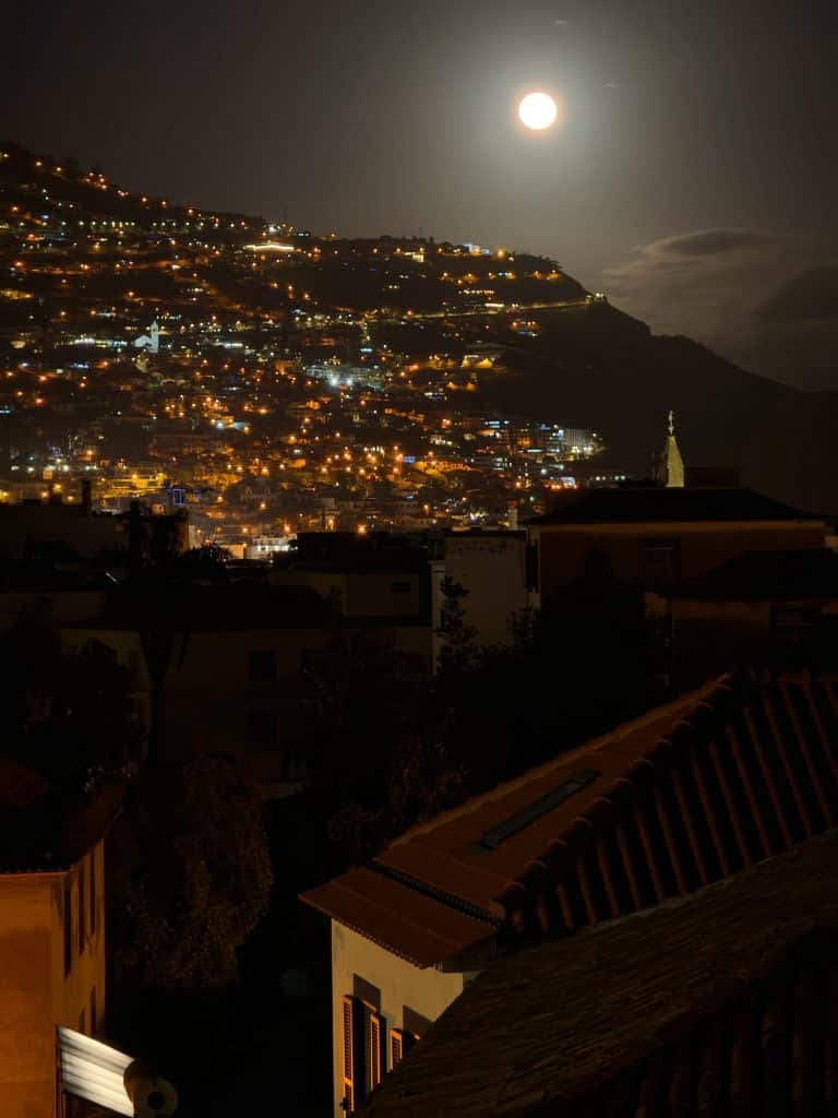 Ein Vollmond über Funchals lichterfülltem Hang, vorne dunkle Dächer