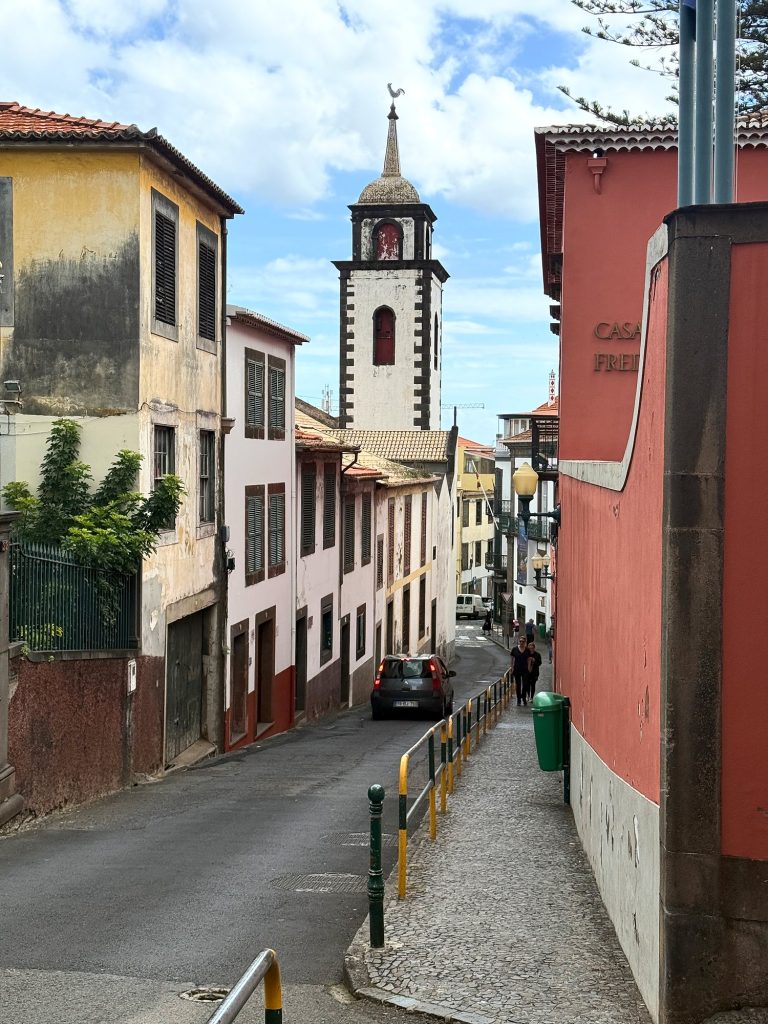 Eine schmale Straße mit alten Stadthäusern und einem roten Haus, am Ende ein weißer Kirchturm