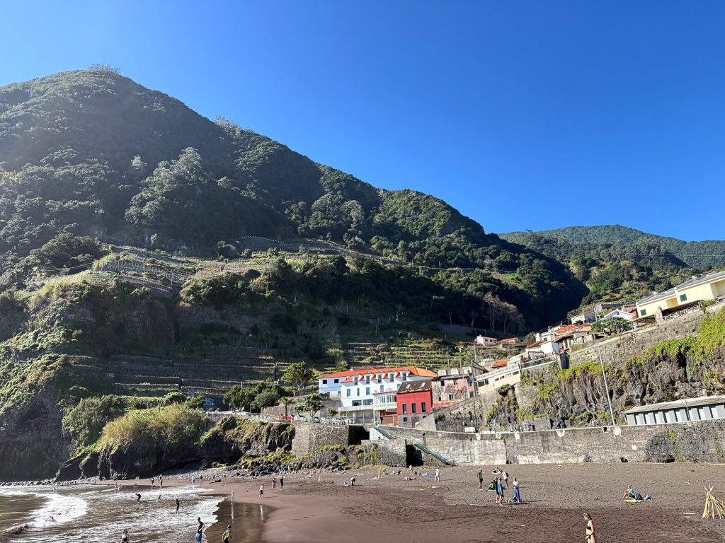 Der schwarze Sandstrand von Seixal unter einem grünen Berg an einem sonnigen Februartag