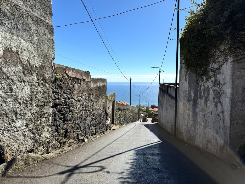 Eine schmale, steile Straße zwischen hohen Steinmauern, am Ende ein Blick auf den Ozean