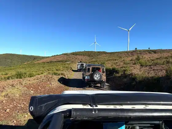 Land Rover auf einer Schotterpiste über die Hochebene Paul da Serra, aus einem offenen Jeep gesehen, dahinter Windräder