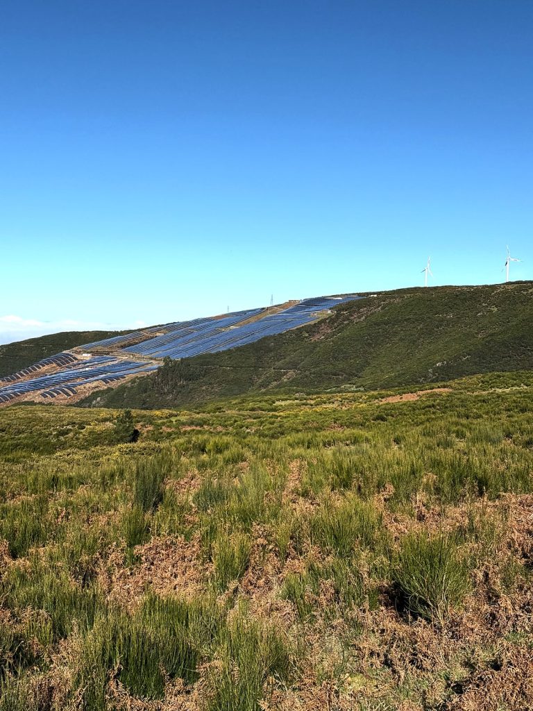 Die Hochebene Paul da Serra mit Gras und Heide, dahinter am Hang Solarmodule und Windräder