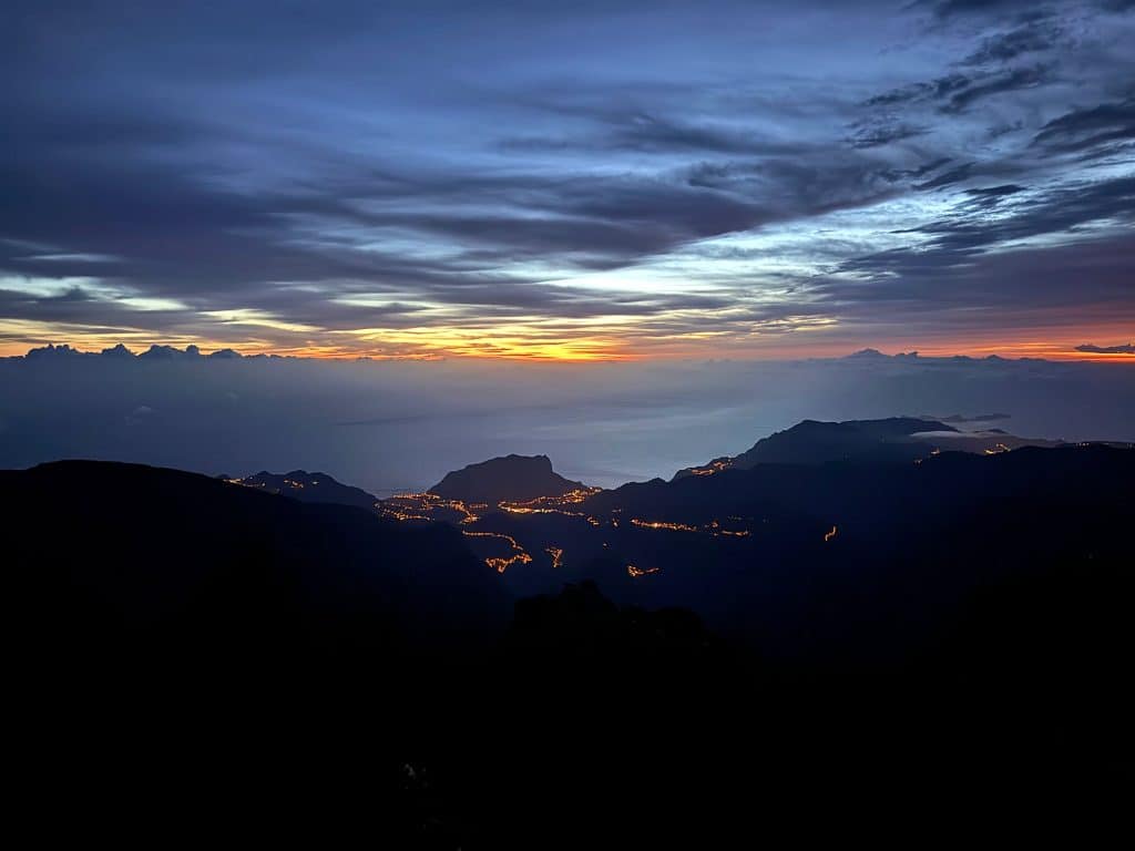 Lichter von Dörfern im Tal und ein orangefarbener Horizont vor Sonnenaufgang auf dem Pico do Arieiro