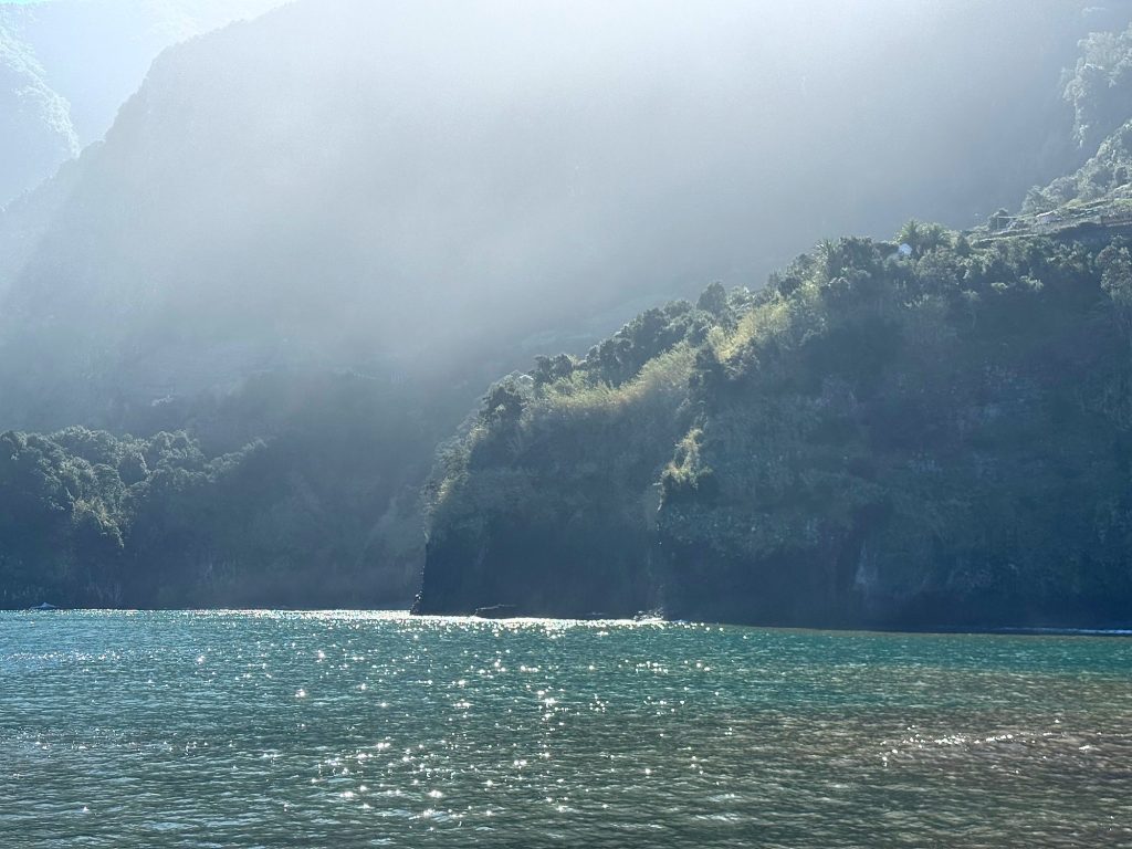 Dunst und grelle Sonne über bewaldeten Klippen, darunter der glitzernde Ozean