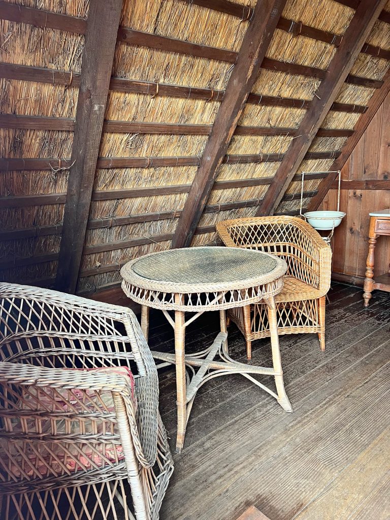 Korbtisch und Korbsessel unter dem schrägen Strohdach im Inneren eines Hauses
