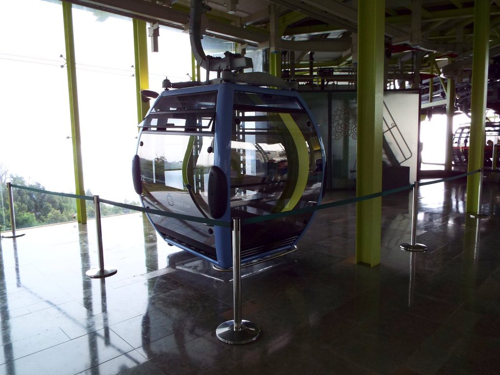 Eine leere blaugraue Seilbahnkabine in der Station, hinter der Scheibe der grüne Hang