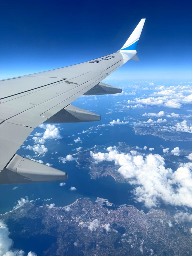 Flugzeugflügel über den Wolken und der Küste, vom Fenster aus gesehen