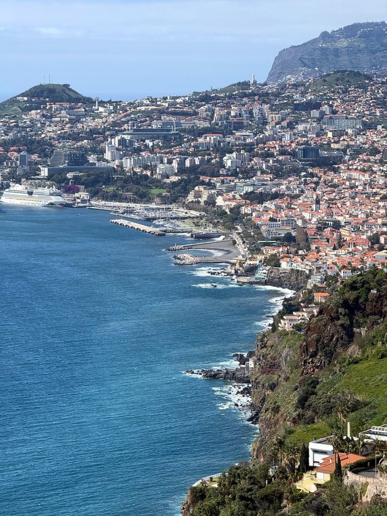 Die Bucht von Funchal mit Hafen, Marina und einem Kreuzfahrtschiff, von einer hohen Klippe östlich der Stadt gesehen, in der Ferne die Klippe Cabo Girão